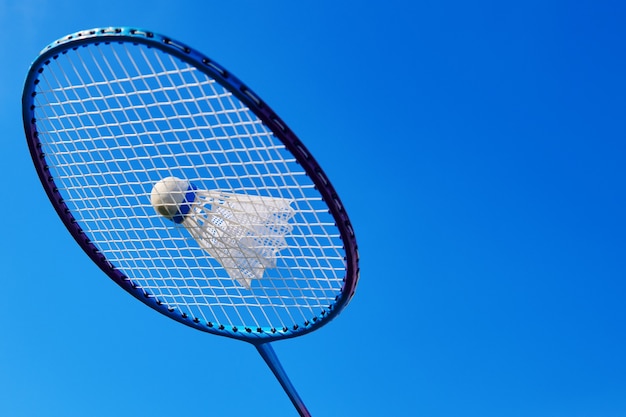 Raqueta de bádminton con volante contra el cielo azul. Actividad de juego de bádminton al aire libre. Deporte al aire libre de bádminton. Vista cercana con espacio de copia.