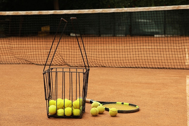 Raqueta y canasta con pelotas en tierra batida