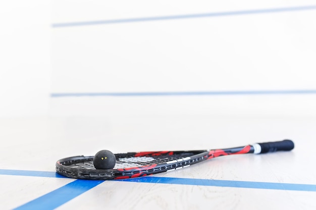 raqueta de squash y pelota en el suelo de madera Equipo de raquetbol en la cancha y pared con líneas en el fondo Foto con enfoque selectivo