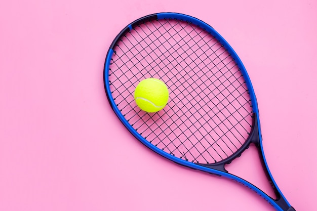 Raqueta de tenis con pelota en superficie rosa