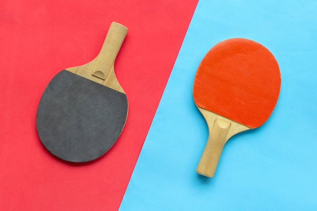 Raquetas de tenis de mesa rojas y negras sobre fondo azul y rojo.