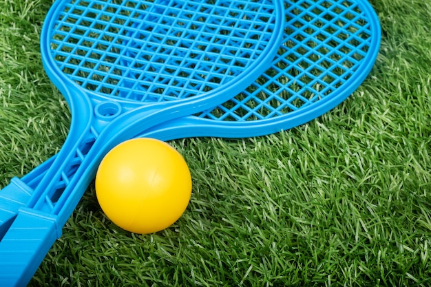 Raquetas de tenis para niños y una pelota sobre césped verde, actividades al aire libre con niños.