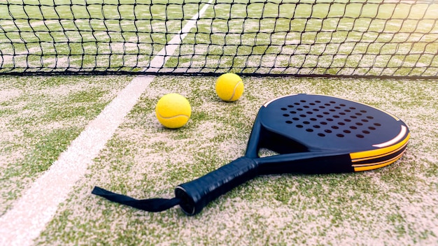 Raquete de padel e bola amarela atrás da rede em um gramado verde ao ar livre