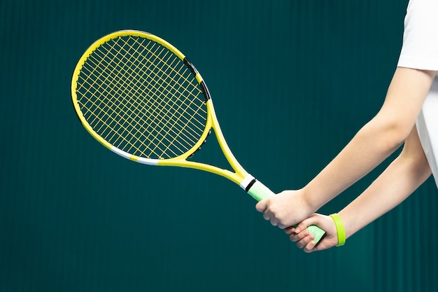 Raquete de tênis nas mãos de uma garota fechada sobre um fundo verde escuro o jogo de tênis