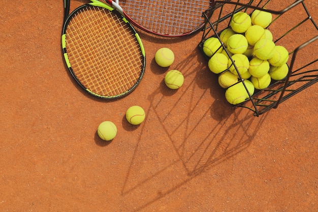 Raquetes e cesto com bolas de tênis em quadra de saibro
