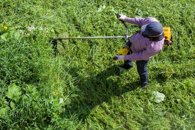 Foto rasenmäher mit stringtrimmer schneidet gras an einem sonnigen tag