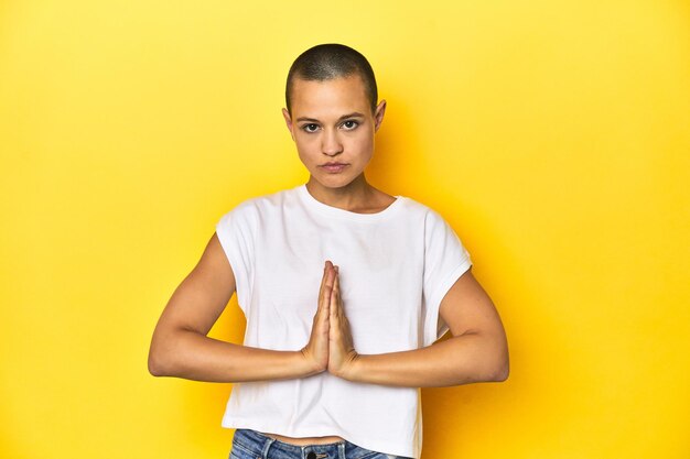 Rasierte Frau mit weißem Tanktop, gelber Hintergrund, betet und zeigt Hingabe