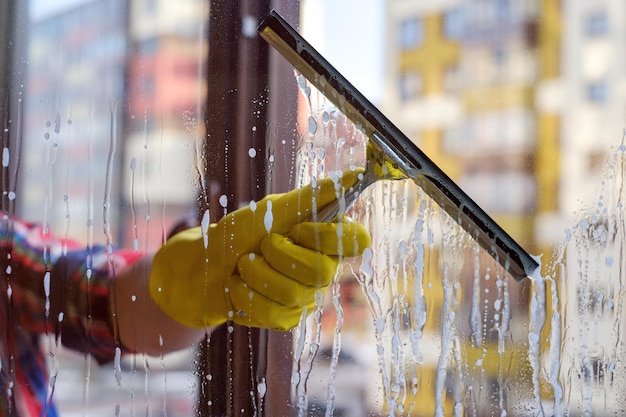Raspador para lavar ventanas en las manos con guantes amarillos Lave las ventanas sucias y polvorientas en primavera