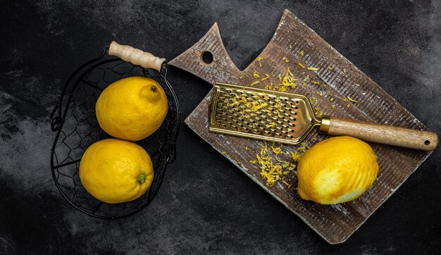 Raspas de limões orgânicos amarelos e ferramenta especial Casca de ralador e raspas de limão no lugar de receita de menu de banner de fundo preto para vista superior de texto