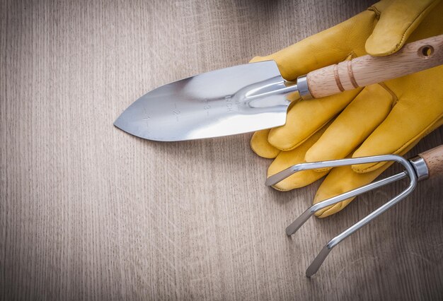 Rastrillo de mano inoxidable rastrillo guantes de jardinería de cuero amarillo sobre tablero de madera concepto de agricultura