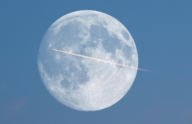 Rastro de avión frente a la luna llena visto con telescopio