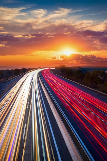 Rastros de luces de autos en la carretera de asfalto Hora de la puesta del sol con nubes y sol Conducir hacia adelante Transportar fondo creativo Movimiento de larga exposición y blurxA