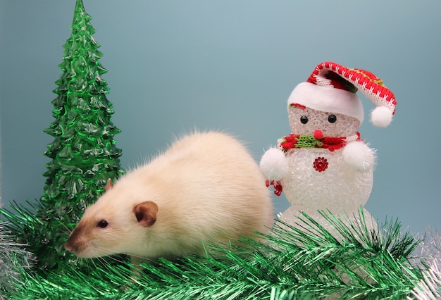 Una rata cerca de un árbol de Navidad de juguete y un muñeco de nieve entre oropel.