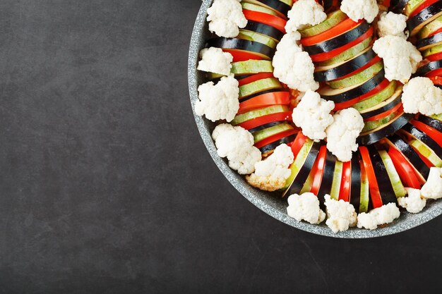 Ratatouille de verduras recién cortadas en una sartén sobre un fondo oscuro