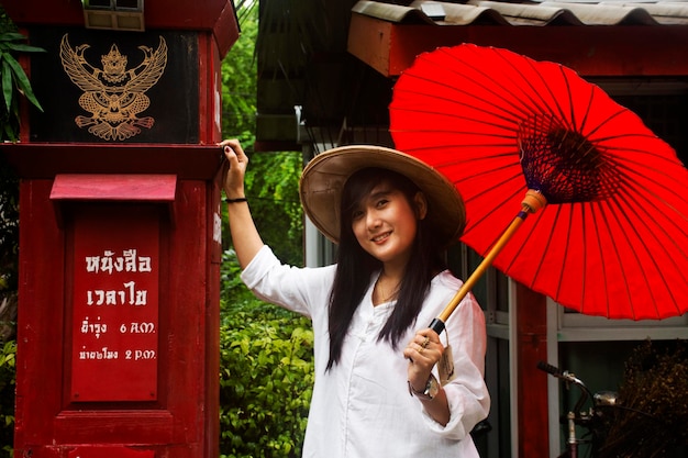 RATCHABURI THAILAND 24. SEPTEMBER Reisende thailändische Frauen tragen Kleidung im vietnamesischen ethnischen Stil mit Bambushut und rotem Regenschirm für ein Foto im Garten am 24. September 2019 in Ratchaburi Thailand