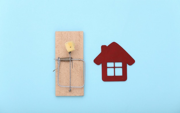 Ratonera con queso y casa sobre fondo azul. La trampa de comprar casa