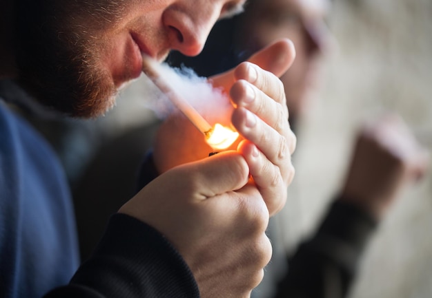 Foto rauchen, drogenmissbrauch, sucht und schlechte angewohnheiten konzept - nahaufnahme von jungen menschen, die im freien eine zigarette anzünden