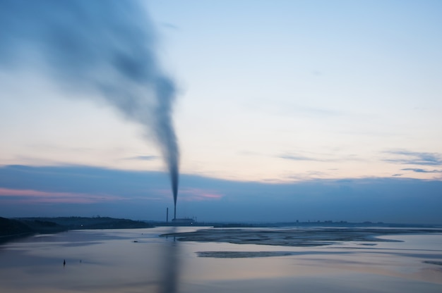 Rauchende Schornsteine in der Nähe des Sees am Abendhimmel.