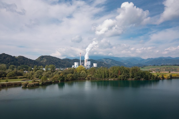 Rauchender Schornstein im Wärmekraftwerk in der Nähe des Sees und Luftaufnahme der grünen Natur