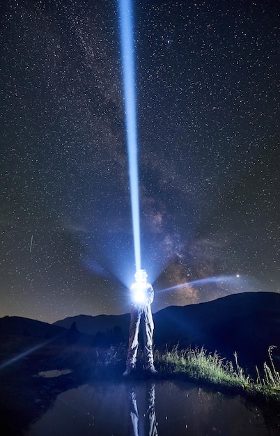 Raumfahrer im Raumanzug lenkt mit Hilfe einer Laterne in der Nacht in den Bergen einen Lichtstrahl in den Himmel