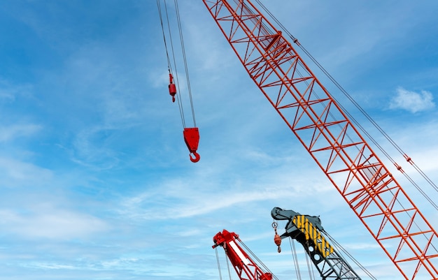 Raupenkran gegen blauen Himmel und weiße Wolken. Immobilienwirtschaft. Roter Raupenkran verwendet Haspel-Hebegeräte auf der Baustelle. Kran zu vermieten. Kranhändler für Bauunternehmen.