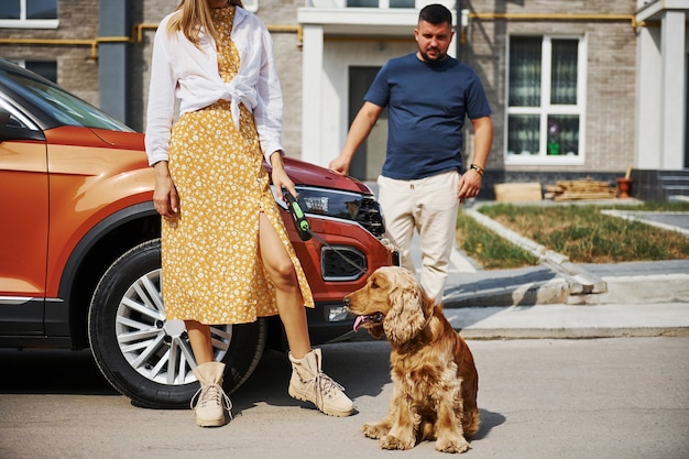 Raus aus dem Gebäude. Schönes Paar geht zusammen mit Hund draußen in der Nähe des Autos spazieren.