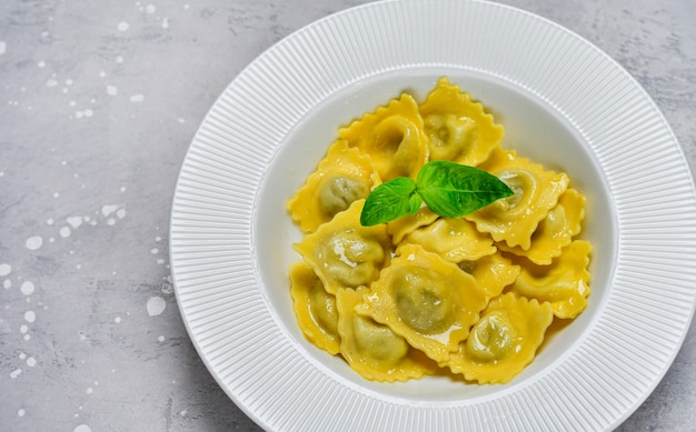 Ravioles con ricotta y espinacas en un plato blanco sobre una mesa de piedra gris. Receta de pasta italiana, almuerzo gourmet. Vista superior