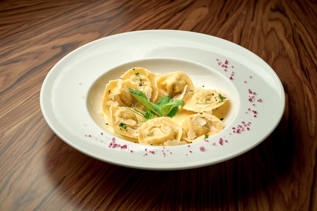 Ravioli com diferentes recheios ao molho e parmesão em prato branco sobre fundo de madeira