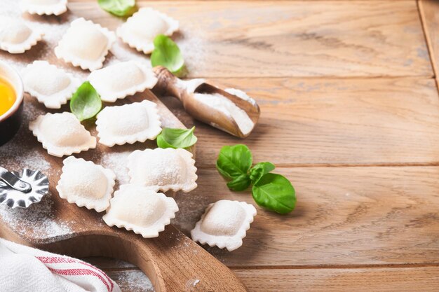 Ravioli Comida italiana Sabrosos raviolis de pasta casera con harina, tomates, huevos y albahaca verde sobre fondo de madera Proceso de elaboración de raviolis italianos Fondo de ingredientes de cocina Vista superior