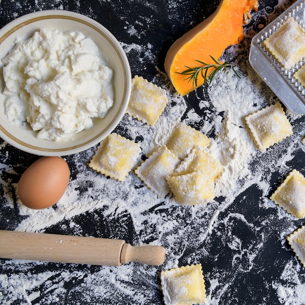 Ravioli crudo tradicional con calabaza en una mesa de madera con harina, hecho a mano, proceso de cocción