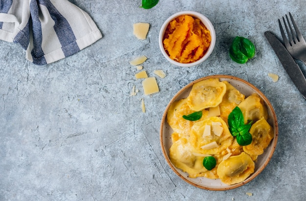 Ravioli de abóbora caseiro com molho e bsil no fundo de concreto. Conceito de comida de outono.