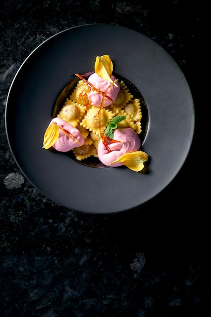 Ravióli doce com cerejas e sorvete rosa servido em um prato preto sobre uma mesa de mármore escuro. Comida do restaurante. Cozinha italiana. Bolinhos com recheio doce