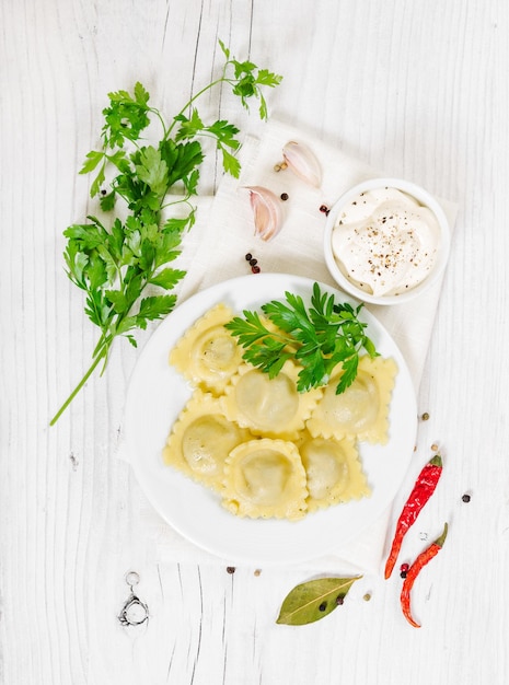 Ravioli italiano cocido en plato blanco sobre fondo rústico de madera blanca