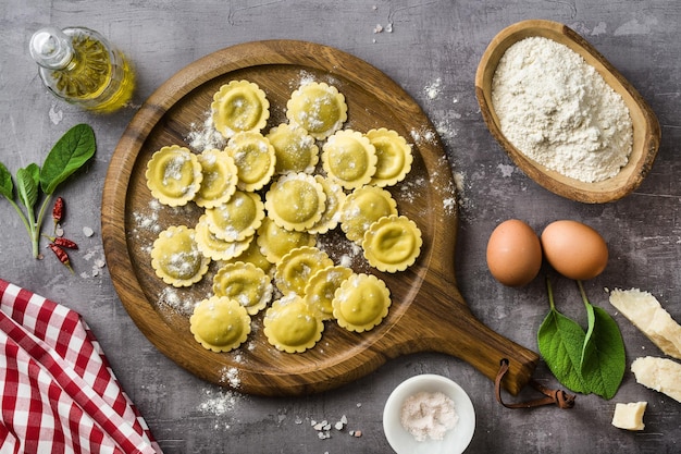 Ravióli italiano cru fresco sobre a mesa com ingredientes para cozinhar em casa