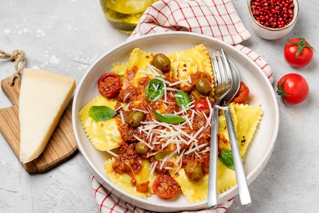 Ravioli de pasta con salsa de tomate y aceitunas con albahaca y queso sobre un fondo gris