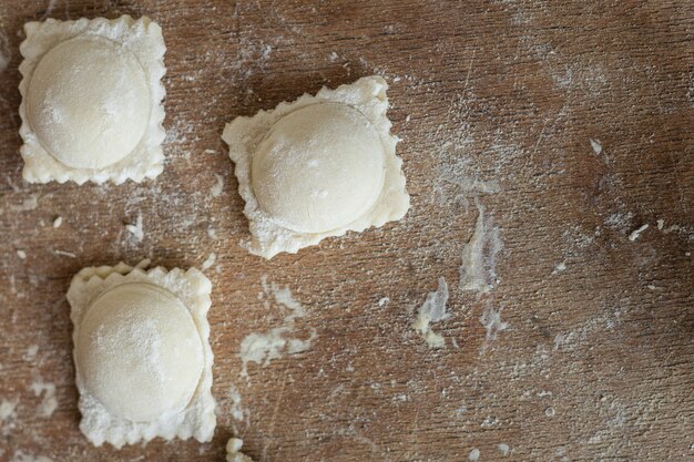 Ravioli roher Teig, der quadratische Knödel auf dem gesunden Mahlzeitkopienraumlebensmittelhintergrund des Tisches füllt