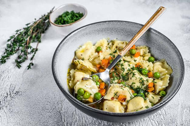 Ravioli-Suppe-Knödel-Nudeln in einer Schüssel mit Grüns. Weißer Hintergrund. Ansicht von oben.