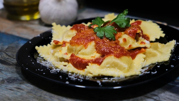 Ravioli con tomate, queso y perejil en un plato negro sobre una madera azul