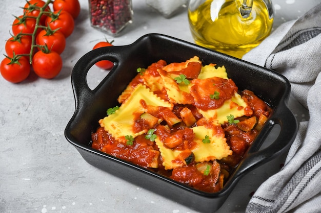 Ravioli-Tomatensauce auf schwarzer Pfanne auf einem Holzbrett.