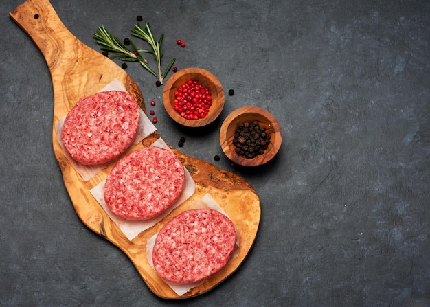 Raw Beef Meat Burger Koteletts und Gewürze auf einem Holzbrett Draufsicht