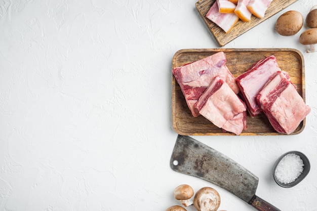 Raw Black Angus Marbled Beef Ribs Set, mit Zutaten und altem Metzger Hackmesser, auf weißem Stein