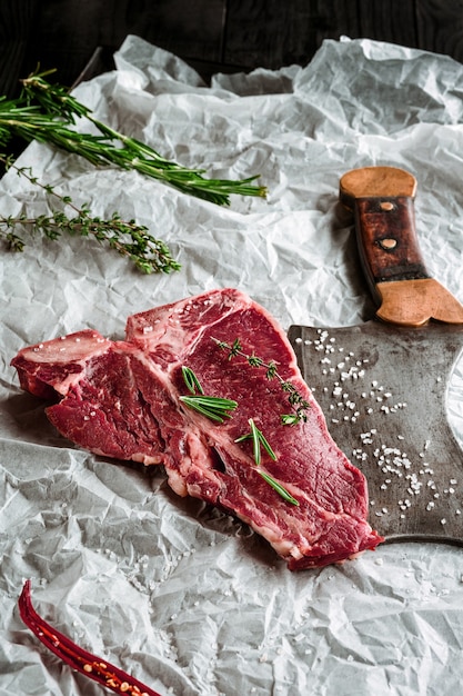 Raw Dry Aged Tbone Steaks zum Grillen mit frischen Kräutern und Hackbeil