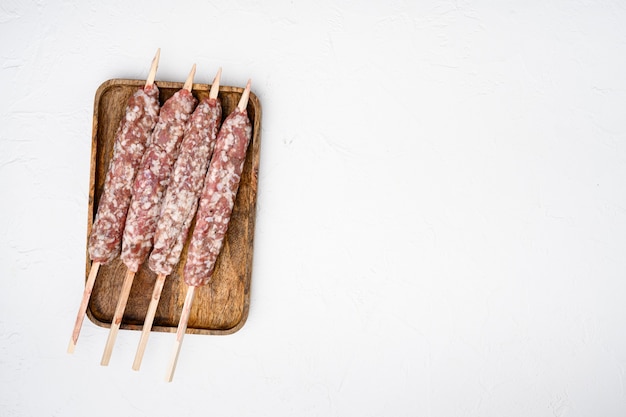 Raw Lula kebab en brochetas, sobre fondo de mesa de piedra blanca, vista superior plana, con espacio para copiar texto