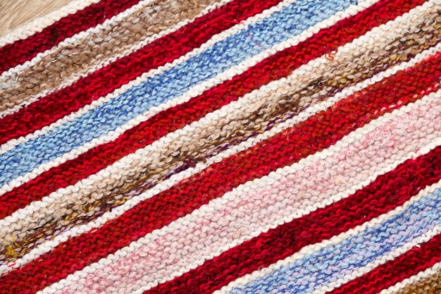 Rayas de diferentes colores en la superficie del tejido de punto. Primer plano de fondo de textiles alfombras o tapetes retro. La textura de la tela es una combinación con la geometría de las líneas. producto artesanal