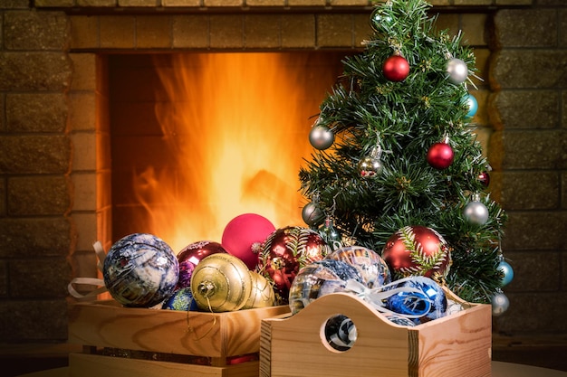 Árbol de año nuevo y cajas con bolas de navidad cerca de la acogedora chimenea en la casa de campo