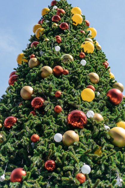 Árbol de navidad adornado con los ornamentos rojos, amarillos y de plata con el fondo brillante del cielo.