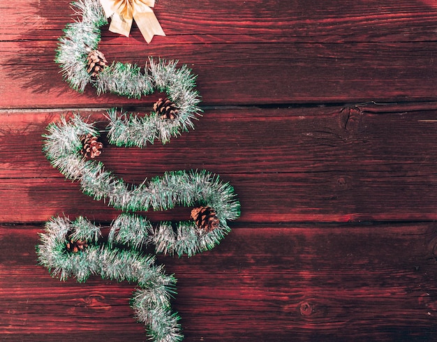 Árbol de Navidad con conos y un lazo dorado en la parte superior sobre un fondo de madera