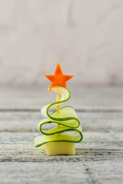 Árbol de navidad creativo de pepino, queso y estrella de zanahoria. Comida divertida para niños para fiesta de año nuevo sobre fondo gris con espacio de copia