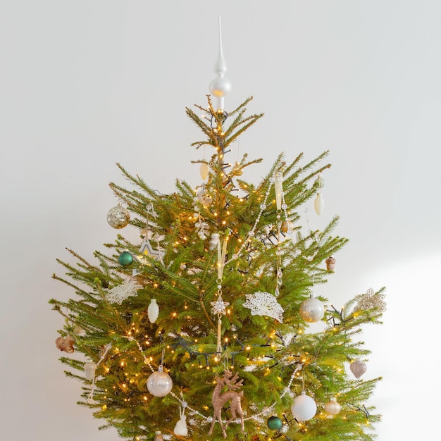 Árbol de navidad con decoración y luces en sala blanca.