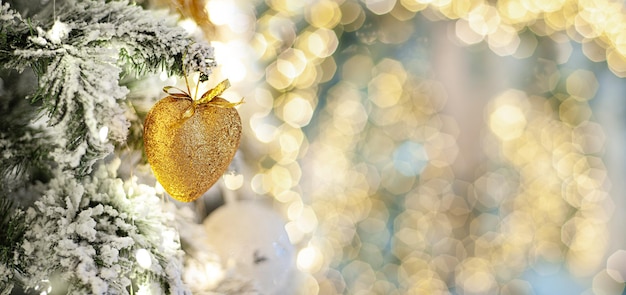 Árbol de Navidad decorado con un corazón de oro. Bandera. Una rama de un árbol cubierto de nieve con decoración navideña con un enfoque suave en el contexto de una guirnalda borrosa. Copie el espacio. Lugar para el texto